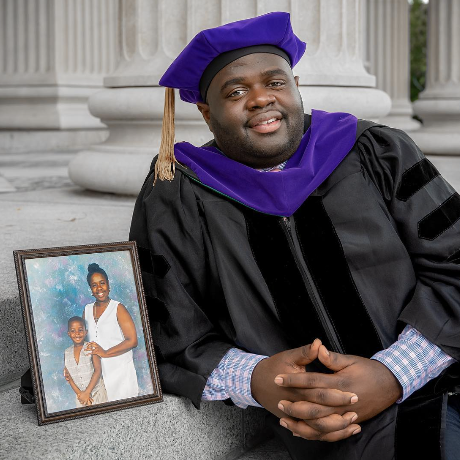 Dr. Kerry Shipman in doctoral regalia with a framed photograph of his mother